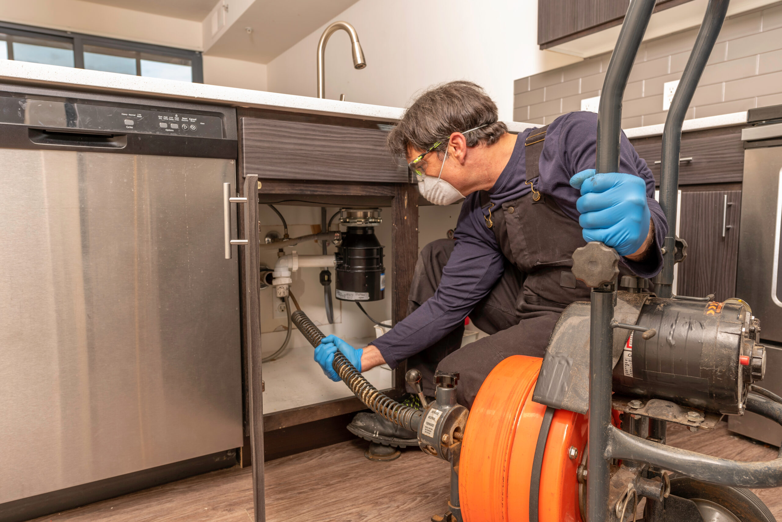 Drain cleaning by professional plumber wearing a safety mask, using an auger